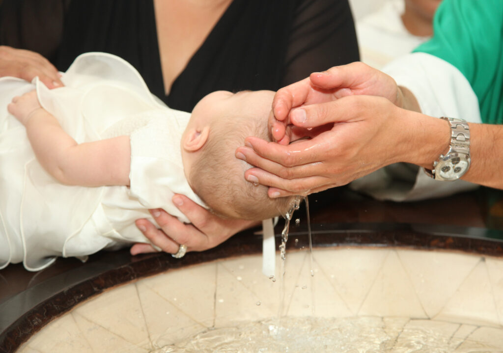 Bebê recebendo o sacramento do batismo, um dos 7 sacramentos.